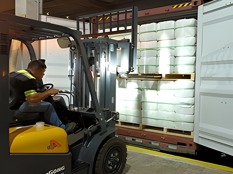 Operador utiliza empilhadeira para carregar fardos em container, durante processo de logística em ambiente industrial.